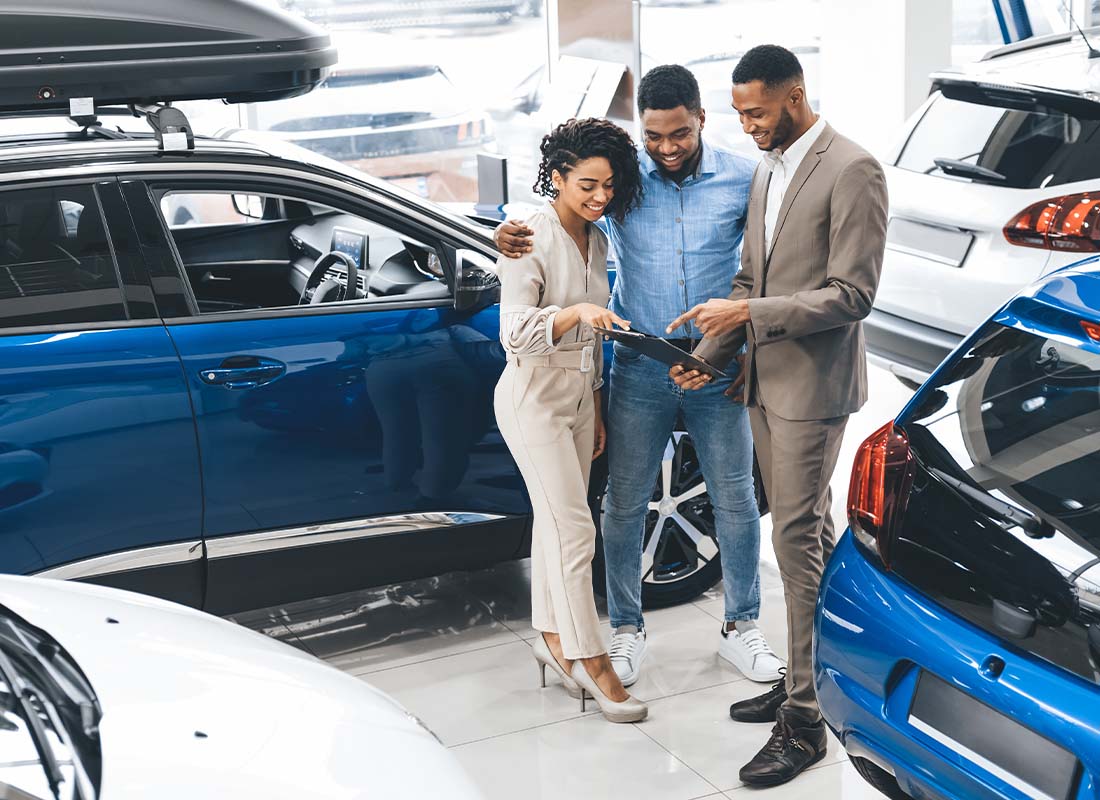 Dealership Insurance - Couple Visiting a Car Dealership and Negotiating with a Salesman in the Auto Showroom before Making a Car Purchase